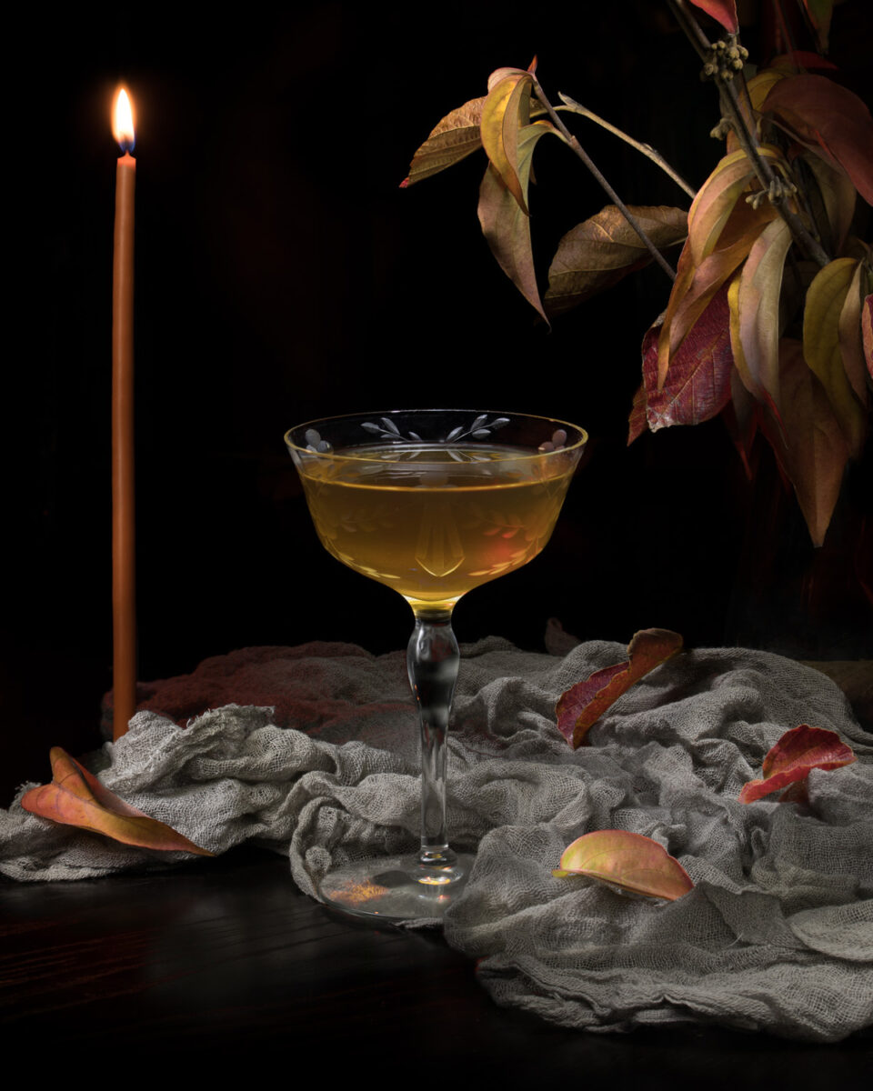 A fall inspired whiskey cocktail with falling leaves and a candle.